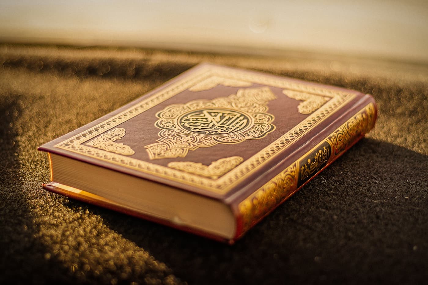 A Qur’an with gold calligraphy resting in soft light.